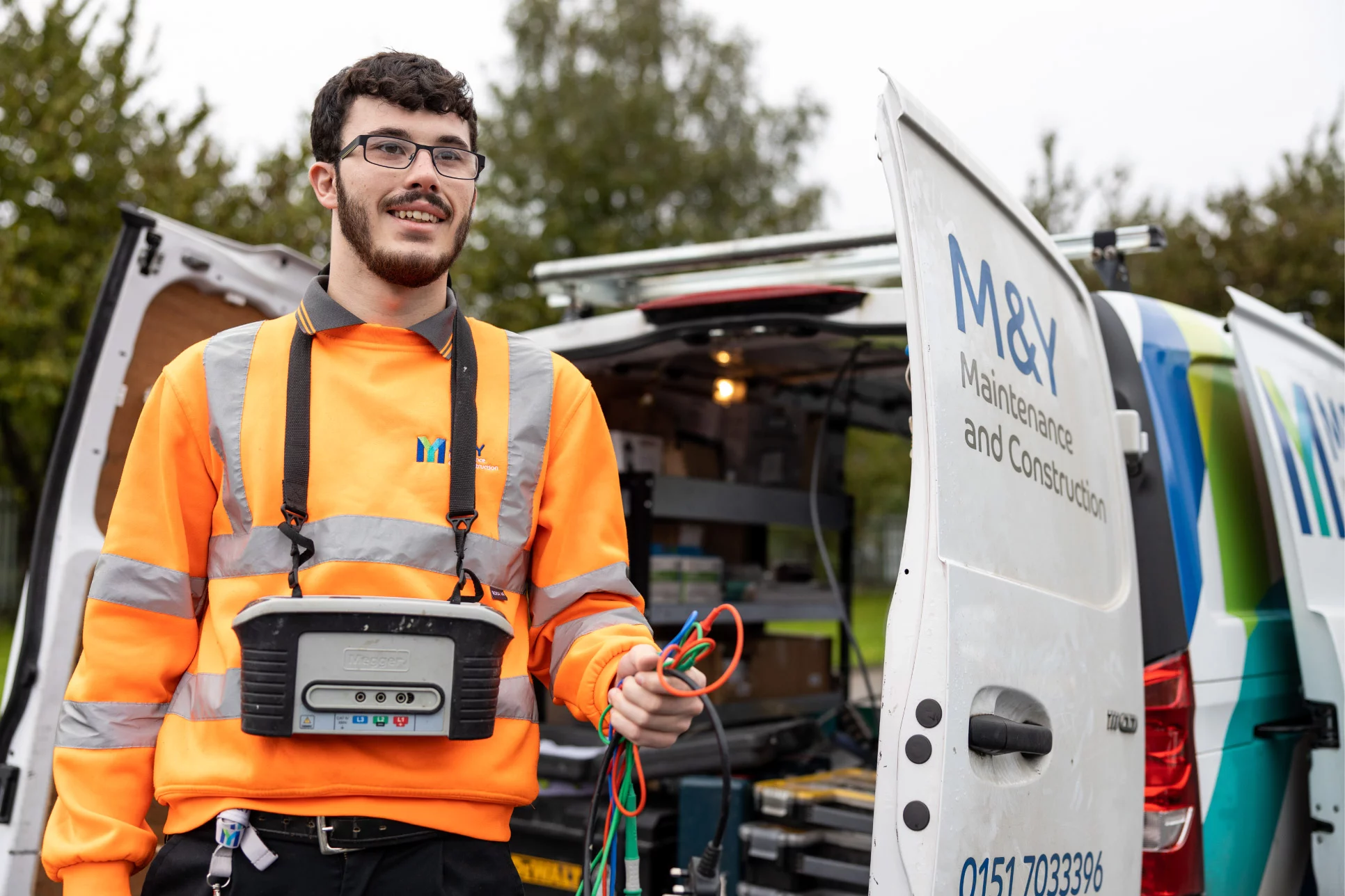 M&Y Operative smiling with electrical testing kit picture next to open M&Y van